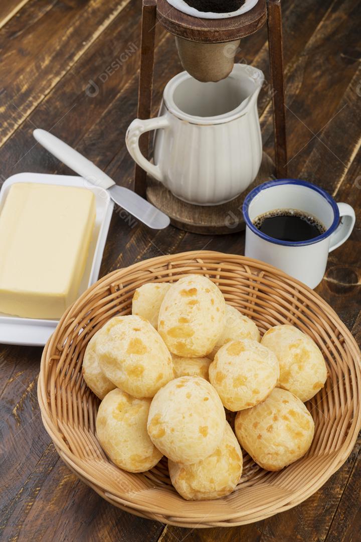 Pão de queijo brasileiro típico em uma cesta com café sobre a mesa de madeira.