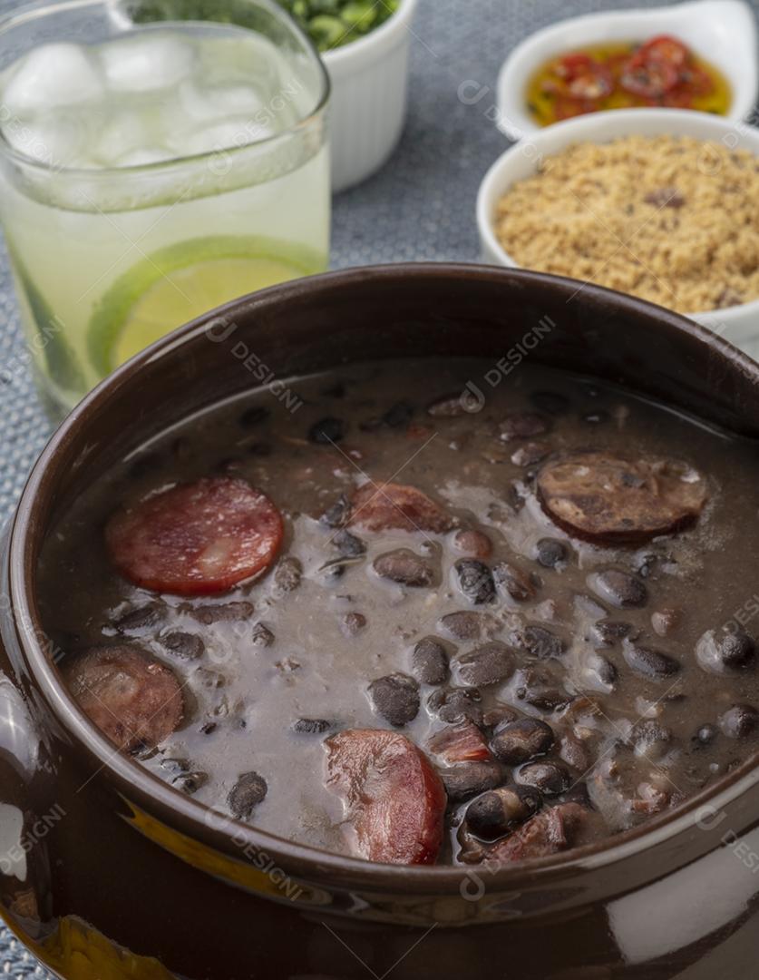 Feijoada tradicional brasileira com couve, pimenta, farinha de mandioca e caipirinha.