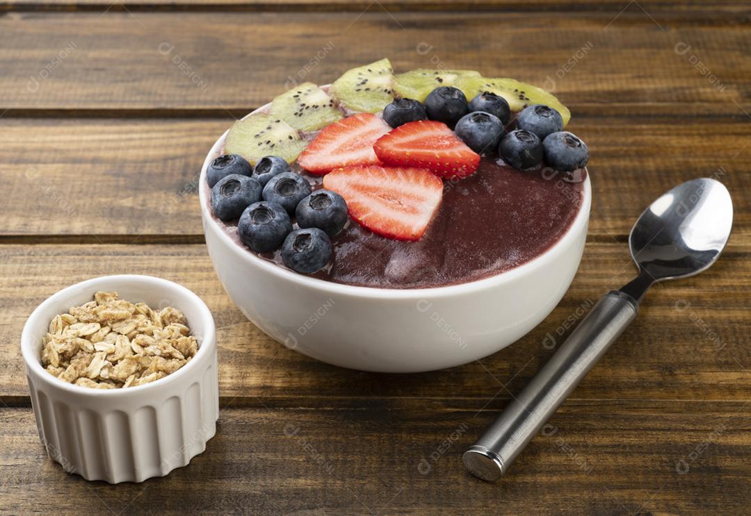 Tigela de açaí típica brasileira com kiwi, mirtilo e morango sobre a mesa de madeira.