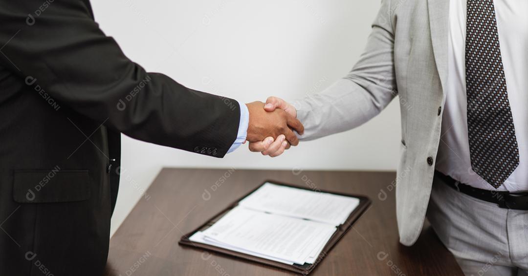 Homens de negócios latinos fazendo aperto de mão após acordo fechado na mesa do escritório.