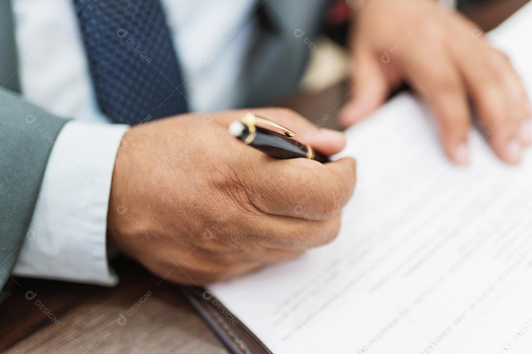Homem de negócios assina documentos com caneta fazendo a assinatura sentado à mesa.