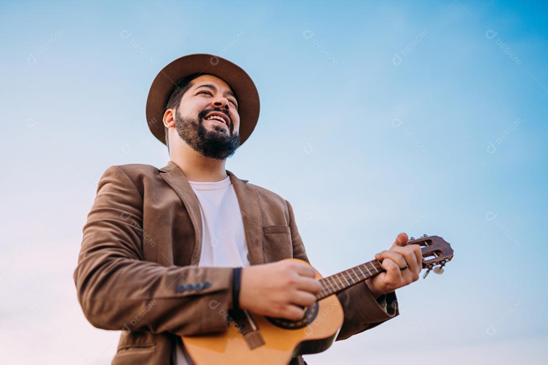 Ao ar livre de um jovem latino-americano tocando cavaquinho ou ukulele. músico brasileiro.