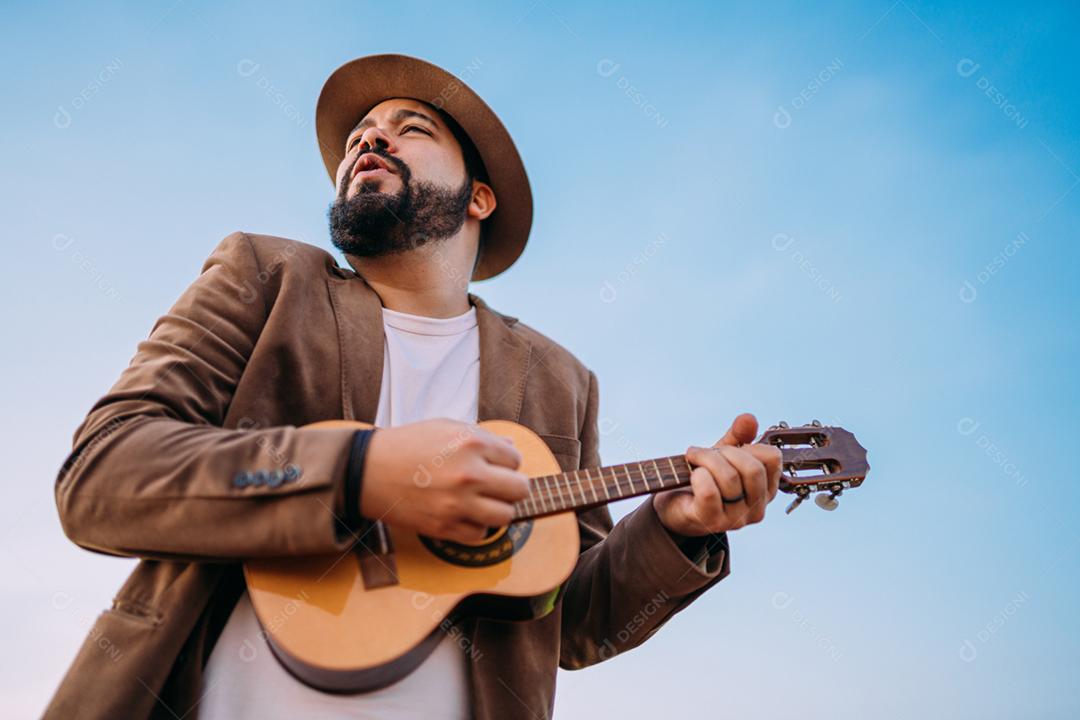 Ao ar livre de um jovem latino-americano tocando cavaquinho ou ukulele. músico brasileiro.