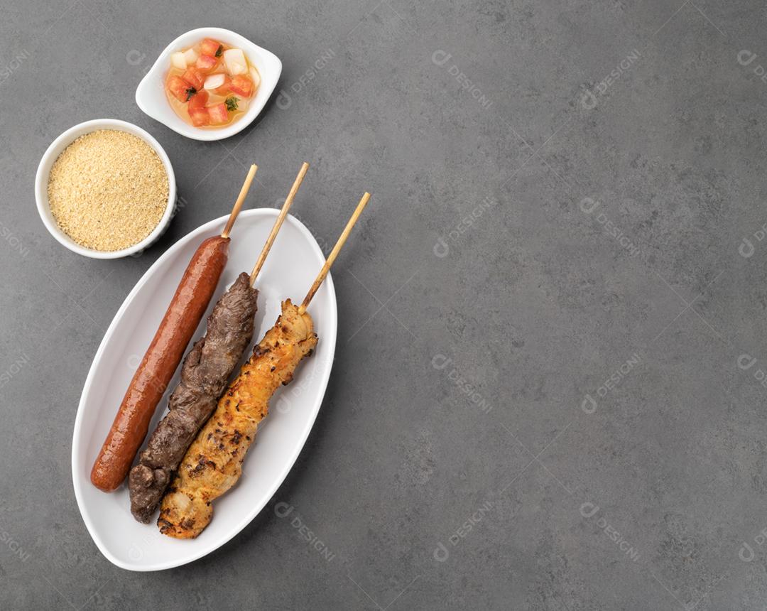 Espetos de linguiça de carne, frango e porco com farofa, vinagrete