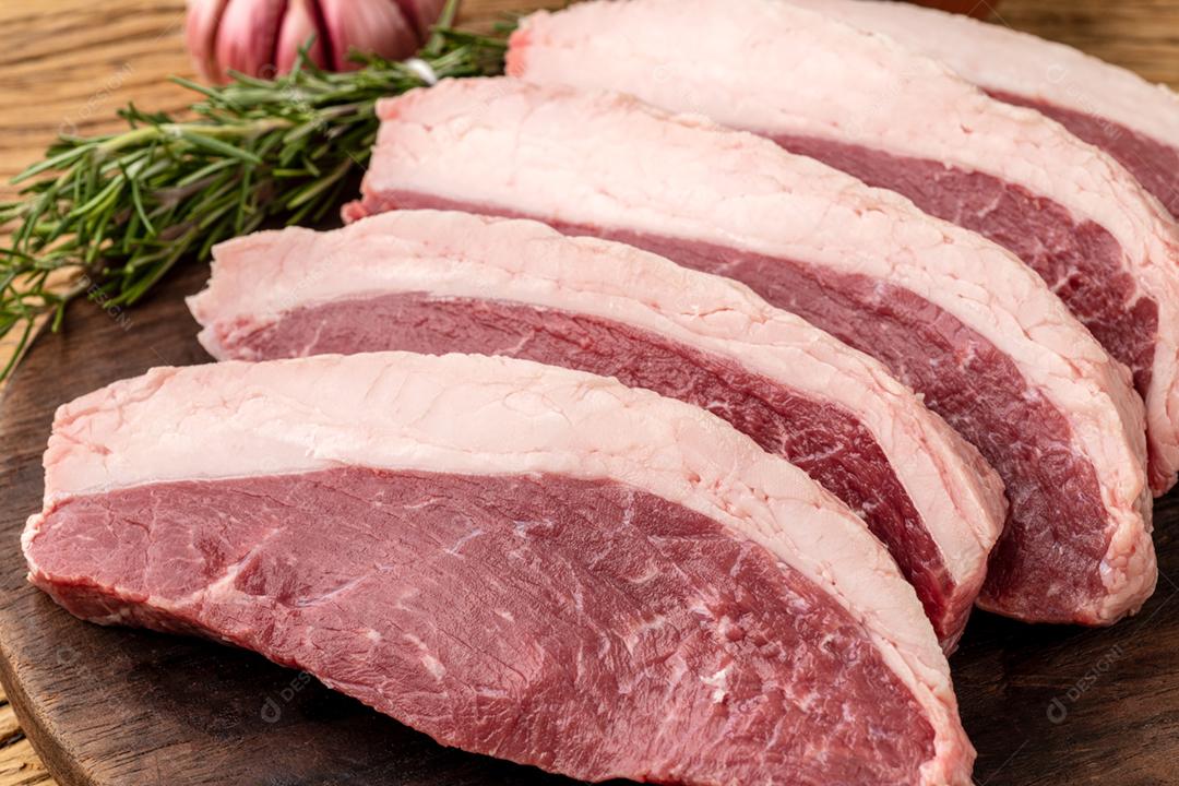 Picanha crua fatiada ou carne de alcatra sobre tábua de madeira com temperos.