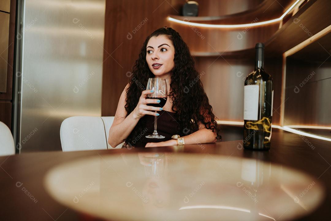 Uma jovem e linda mulher latina mesa segurando copo de vinho tinto em casa sozinha sorrindo