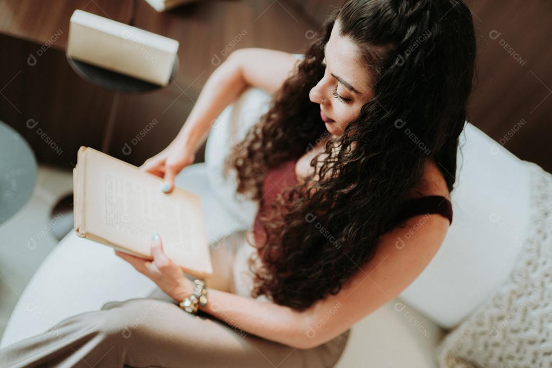 Uma garota latina lendo um livro no sofá em casa.