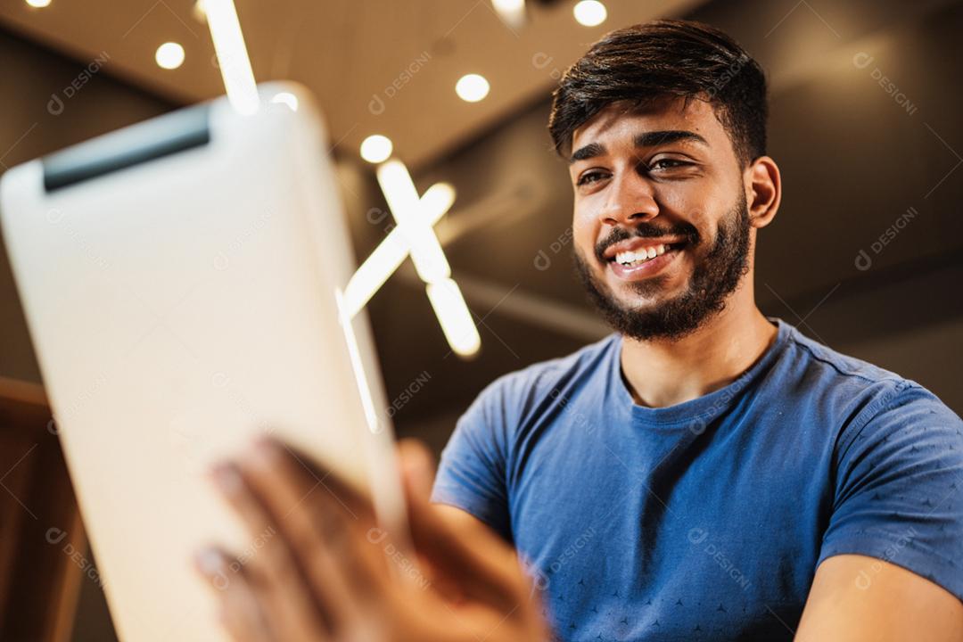 Jovem latino usando tablet digital. Mensagens de texto no café.