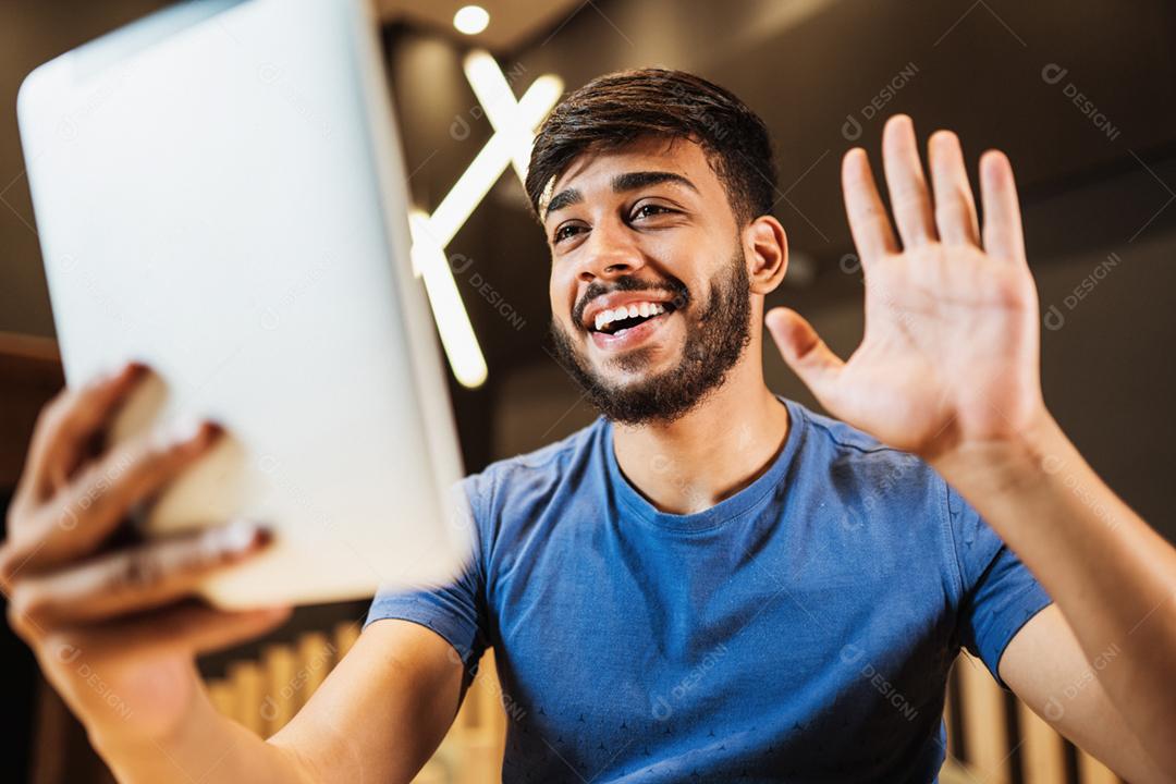 Jovem latino fazendo uma chamada de vídeo no café.