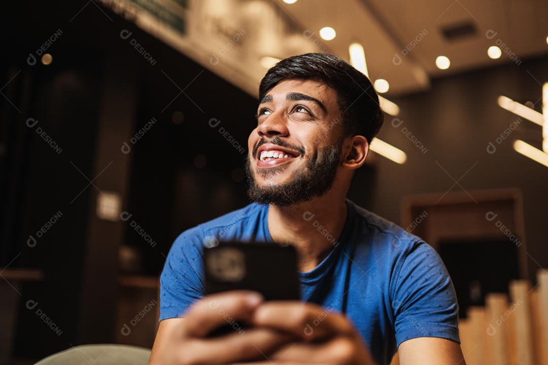Jovem latino usando telefone celular. Mensagens de texto no café.