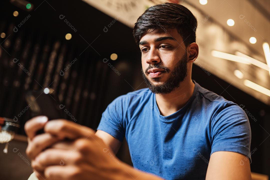Jovem latino usando telefone celular. Mensagens de texto no café.