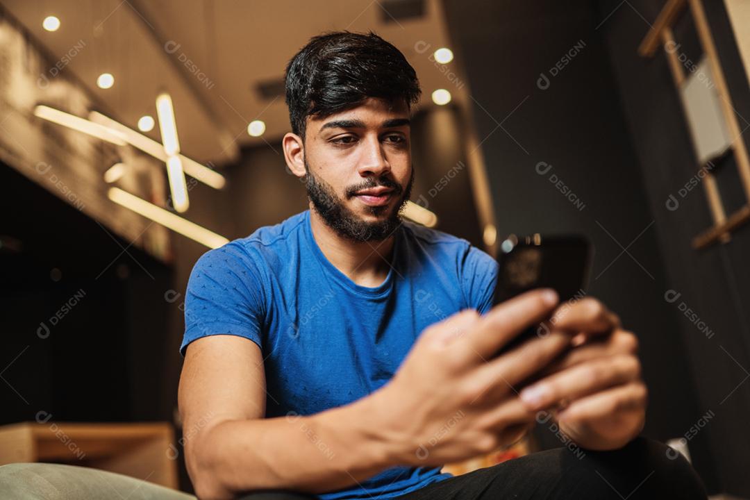 Jovem latino usando telefone celular. Mensagens de texto no café.
