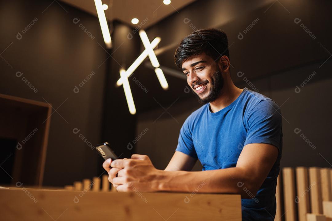 Jovem latino usando telefone celular. Mensagens de texto no café.