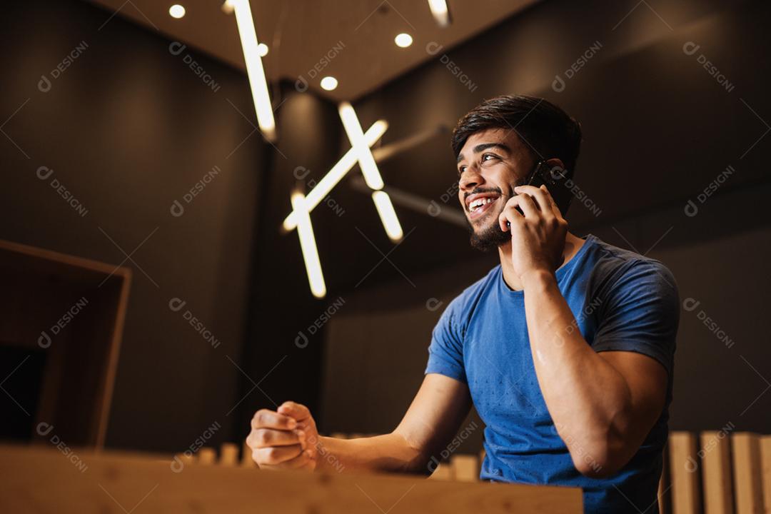 Jovem latino usando telefone celular. Mensagens de texto no café.