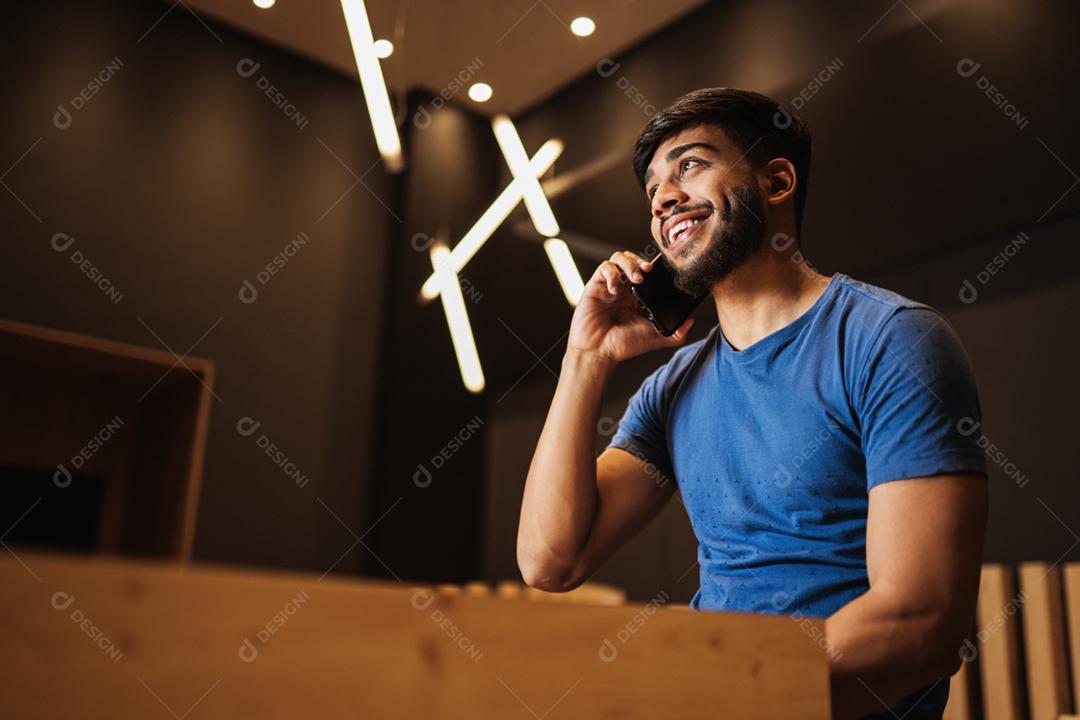 Jovem latino usando telefone celular. Mensagens de texto no café.