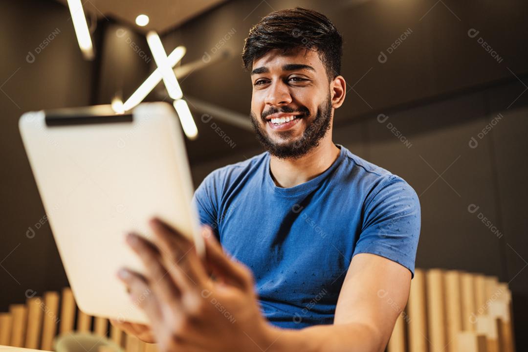 Jovem latino usando tablet digital. Mensagens de texto no café.