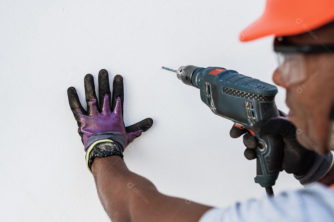 Homem latino confiante segurando broca na parede.