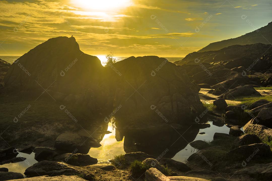 Paisagem por do sol praia pedreiras pedras rochas lago céu nublado