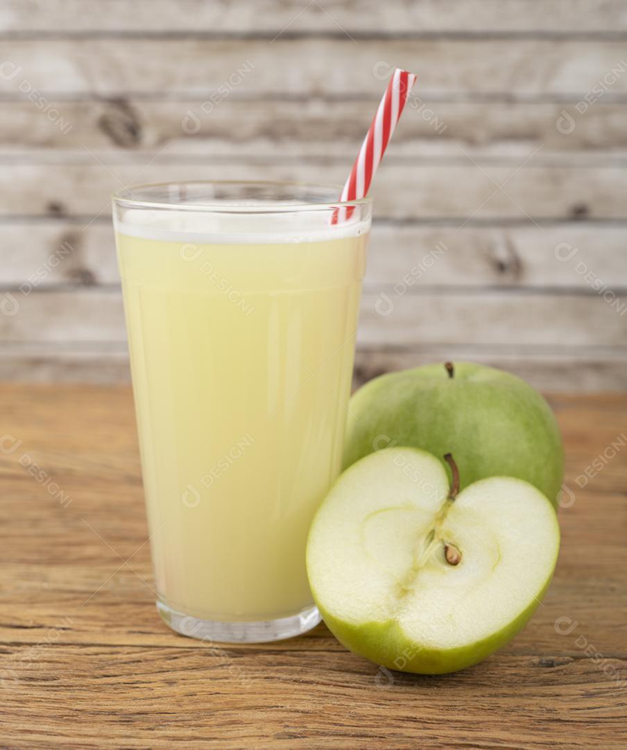 Suco de maçã verde em um copo com frutas sobre a mesa de madeira.