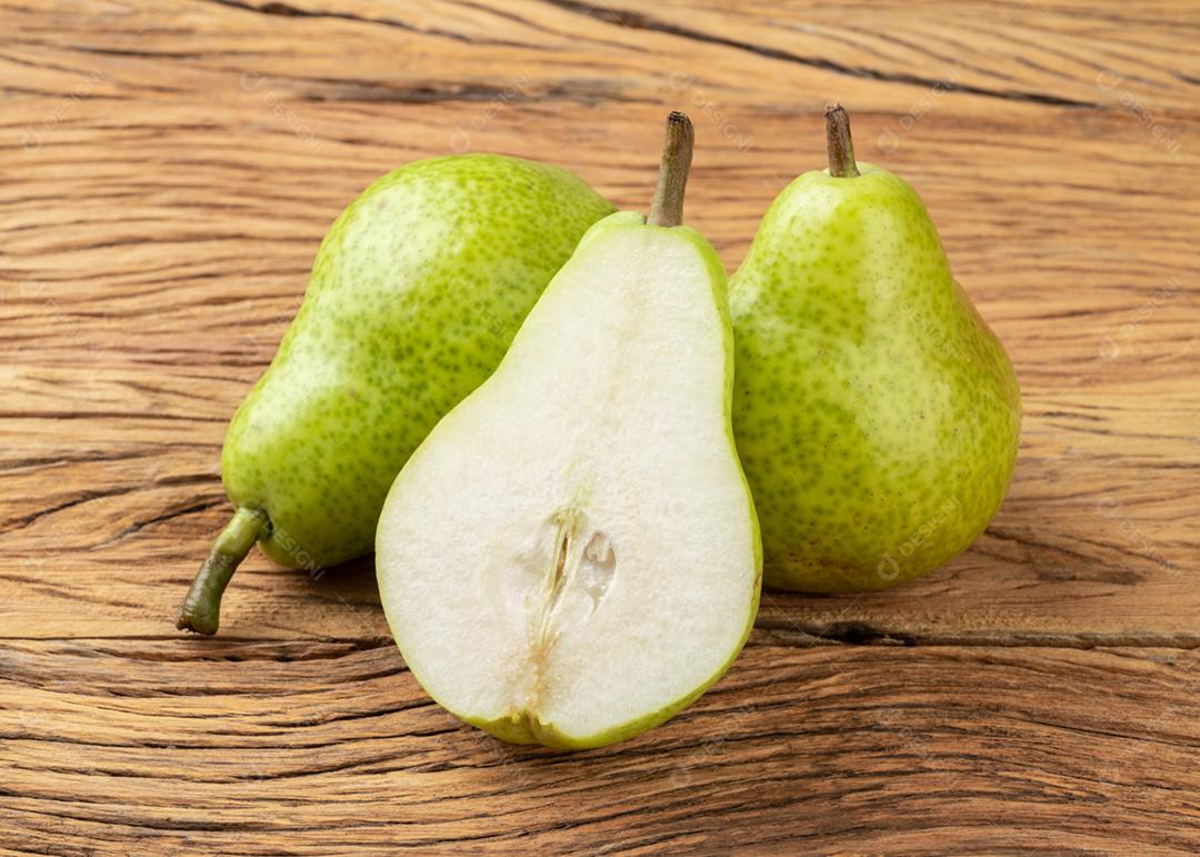 Peras verdes com frutas cortadas sobre a mesa de madeira.