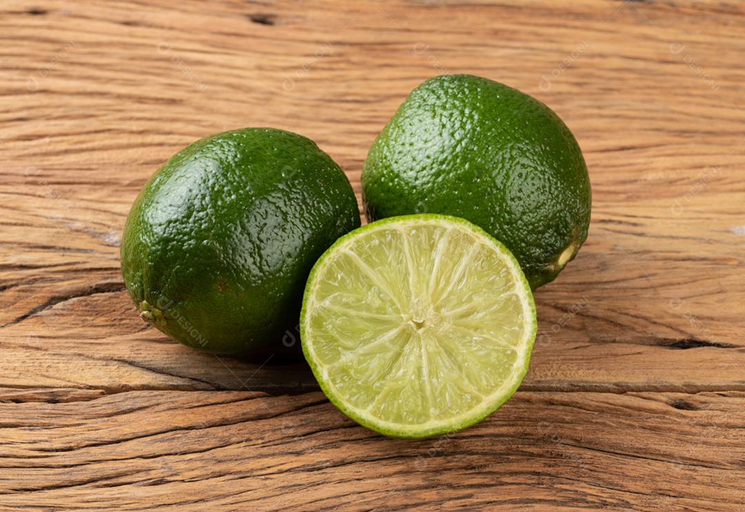 Limão verde e frutas cortadas sobre a mesa de madeira.