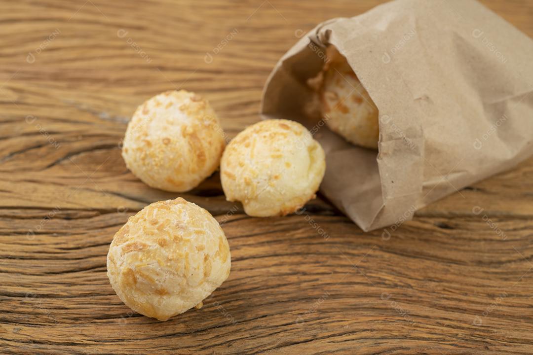 Pão de queijo brasileiro típico em um saco de papel sobre uma placa de madeira.