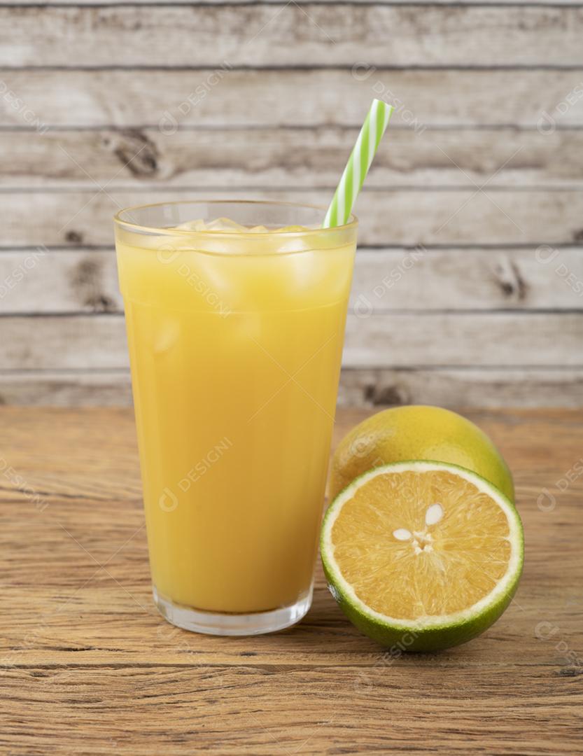 Suco de laranja em um copo com gelo e frutas sobre a mesa de madeira.