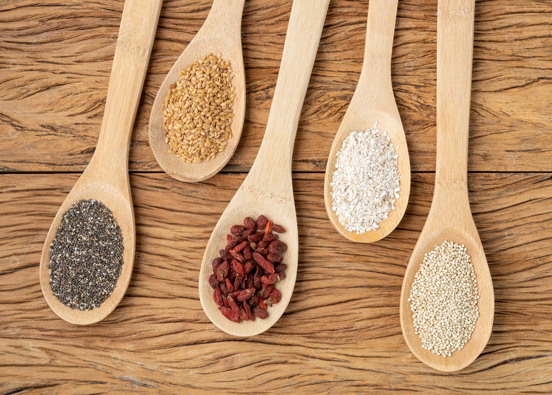 Superalimentos variados em colheres sobre a mesa de madeira. Chia, quinoa, aveia, linhaça e goji berry.