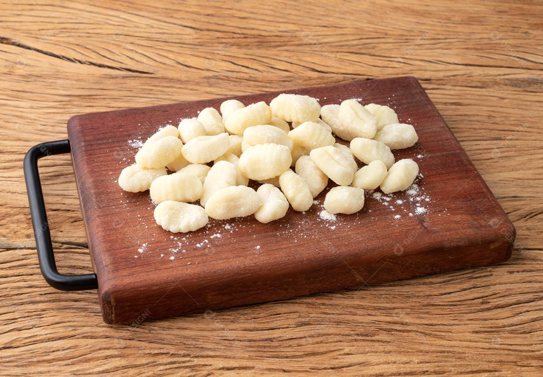 Nhoque de macarrão italiano cru em uma placa sobre a mesa de madeira.