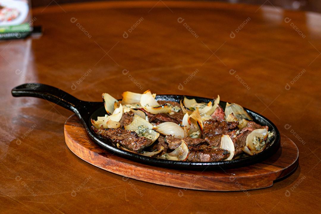 Carne frita cebola sobre frigideira a sobre mesa de madeira