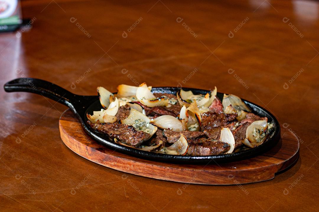 Carne frita cebola sobre frigideira a sobre mesa de madeira