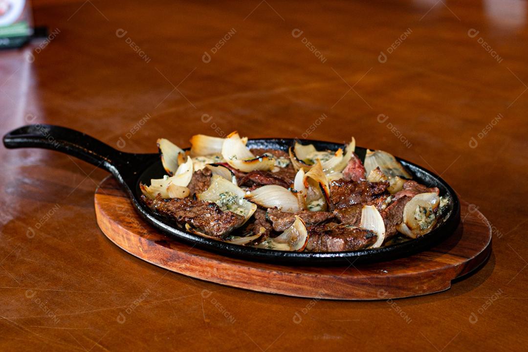 Carne frita cebola sobre frigideira a sobre mesa de madeira