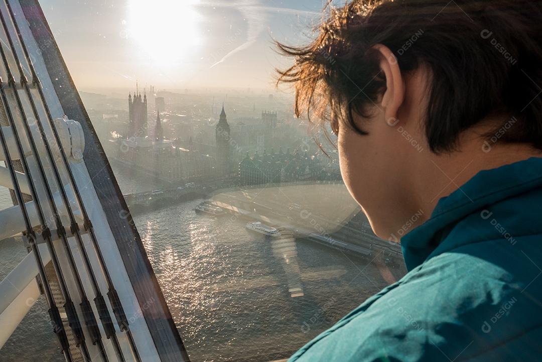 Menino dentro da London Eye com a cidade de Londres ao fundo