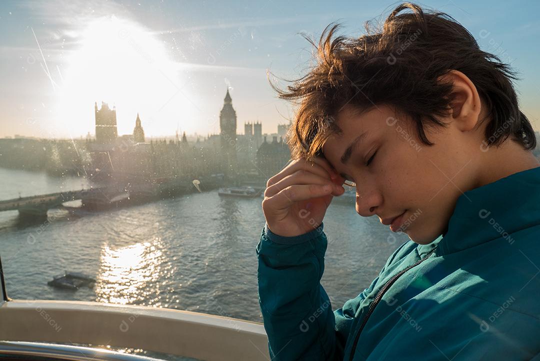 Menino dentro da London Eye com a cidade de Londres ao fundo