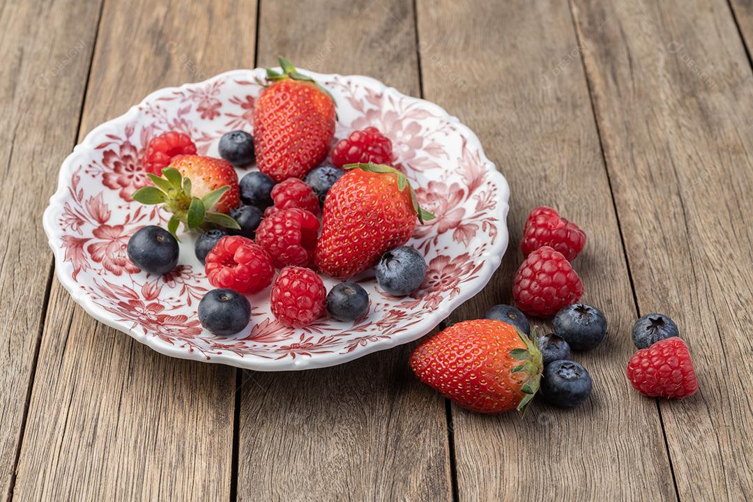 Raspberries, strawberries and blueberries in a plate on wood