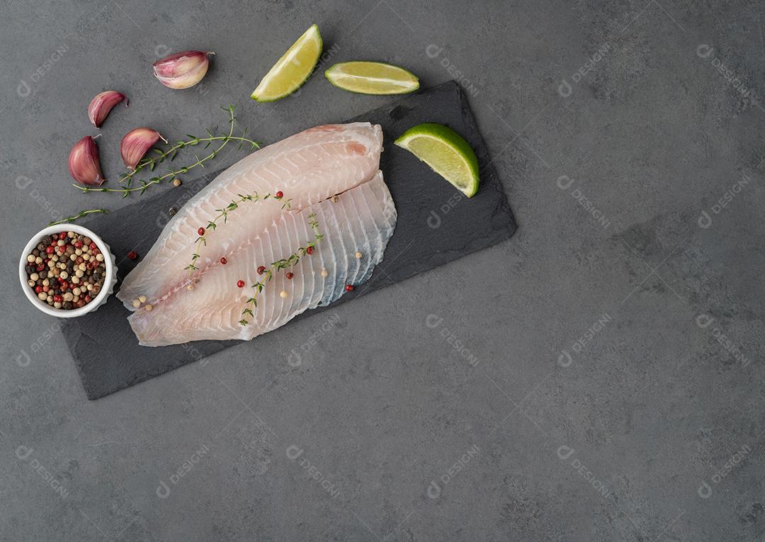 Filé de peixe de tilápia crua com temperos sobre fundo de pedra