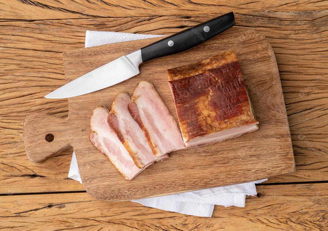 Bacon defumado com fatias e faca sobre tábua de madeira