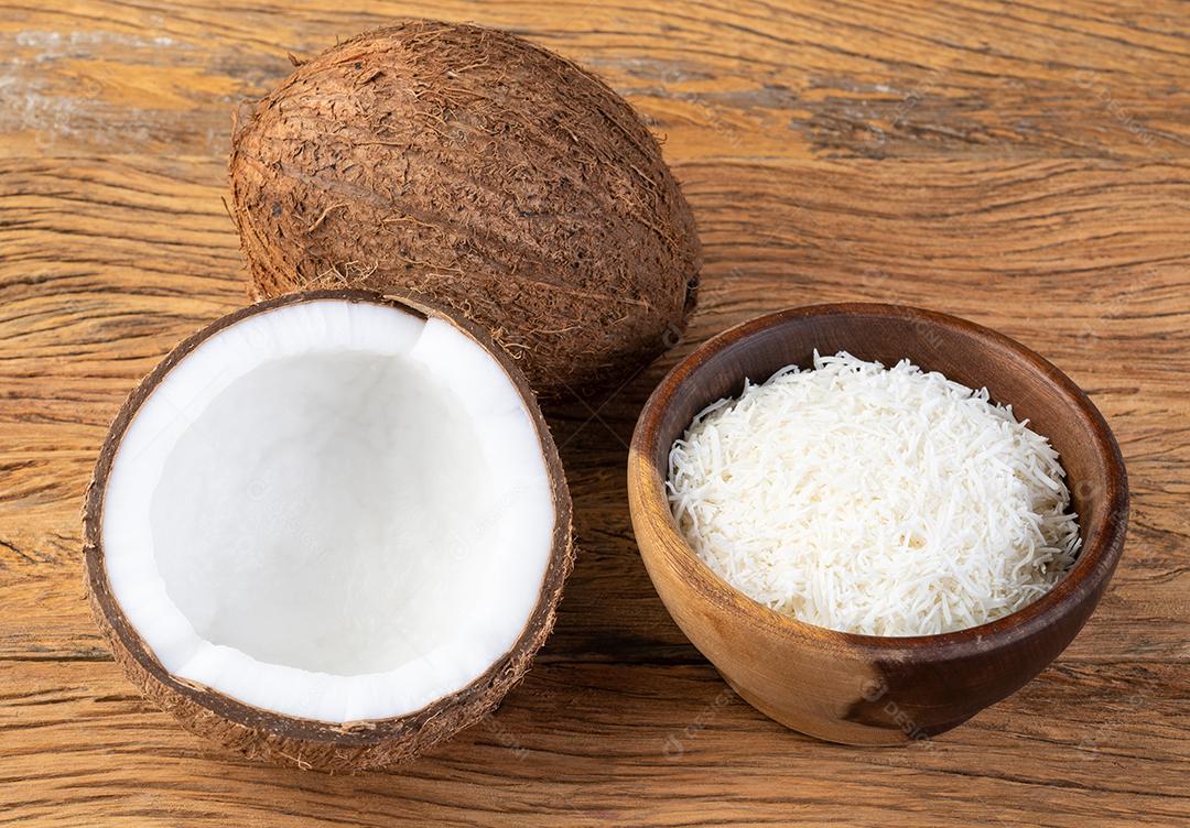Shredded coconut flakes in bowl with berries on wooden table