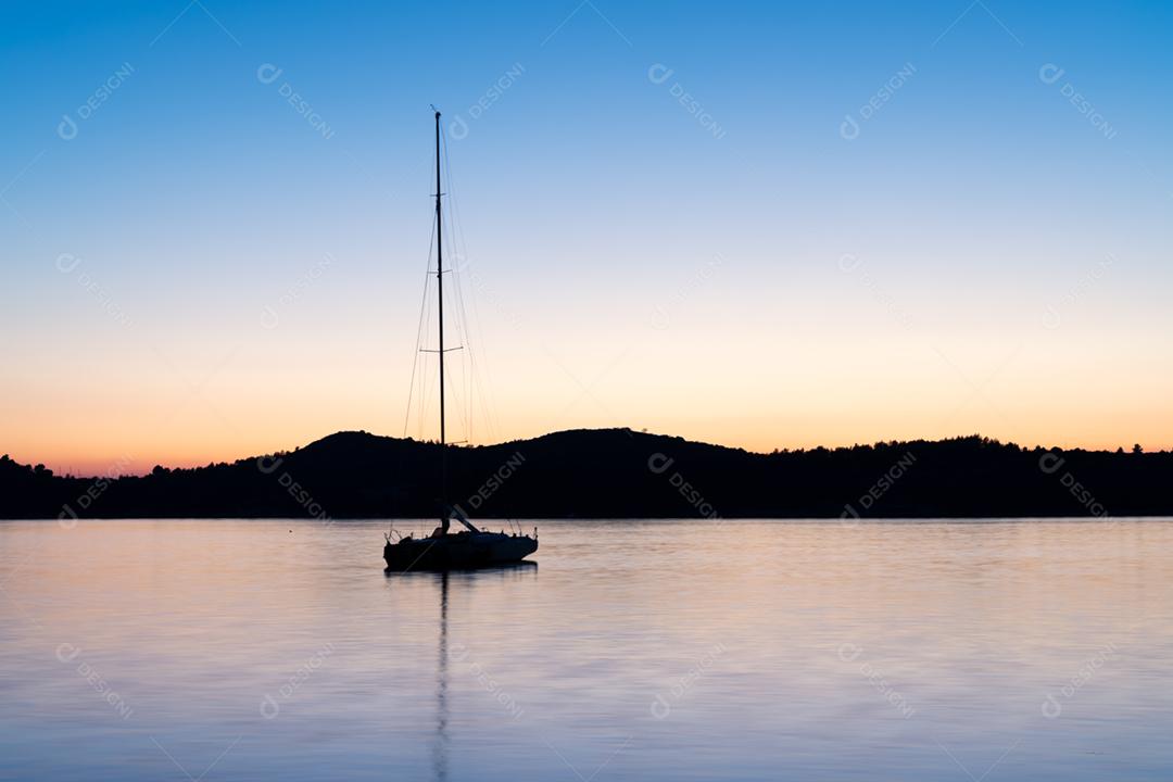 Veleiro nas águas calmas da baía ao pôr do sol