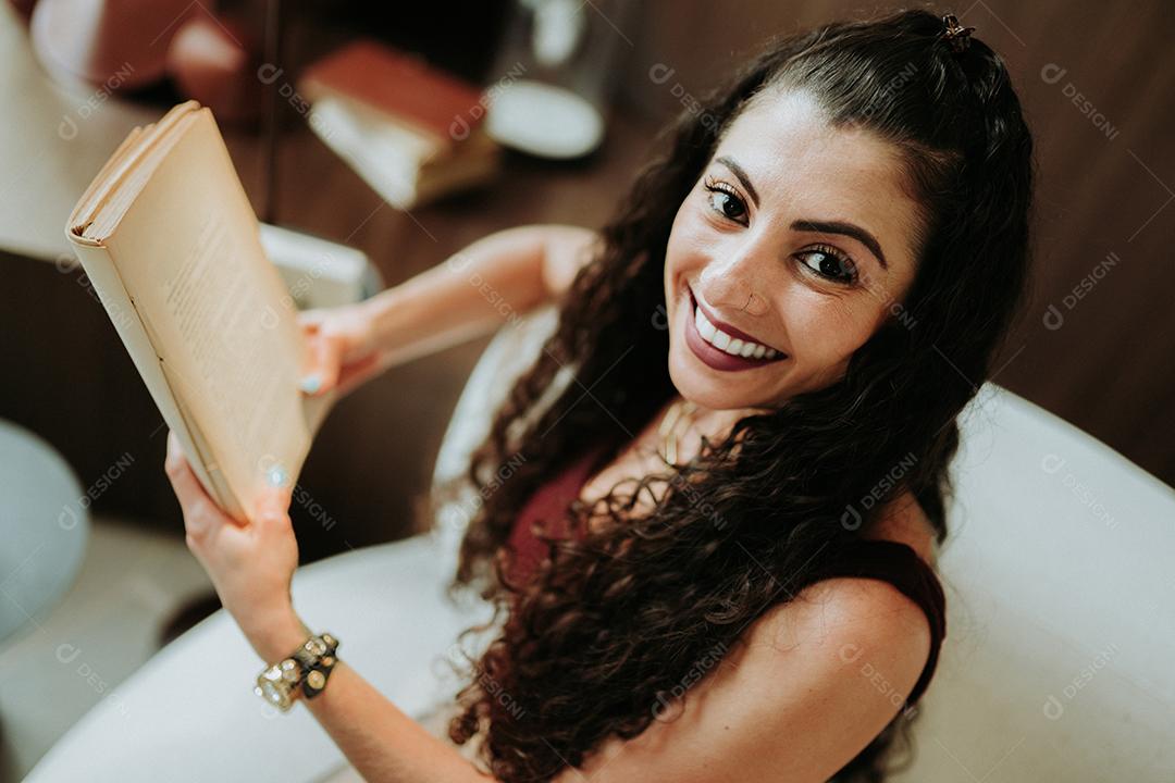 Uma garota latina lendo um livro no sofá de casa.