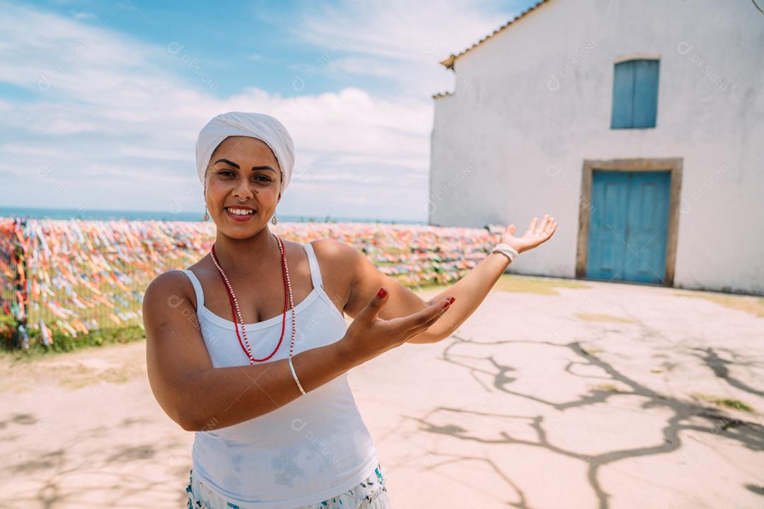Feliz mulher brasileira vestida com traje tradicional baiano, braços cruzados no centro histórico de Porto Seguro ao fundo