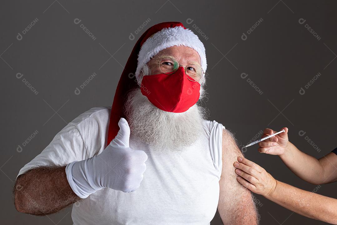 Papai Noel usando máscara facial sendo vacinado com injeção