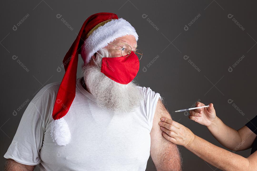 Papai Noel usando máscara facial sendo vacinado com injeção