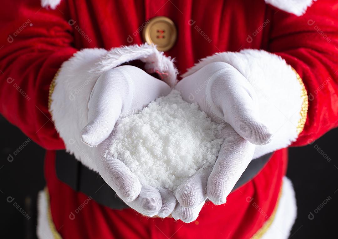 As mãos do Papai Noel segurando um punhado de flocos de neve em suas mãos.