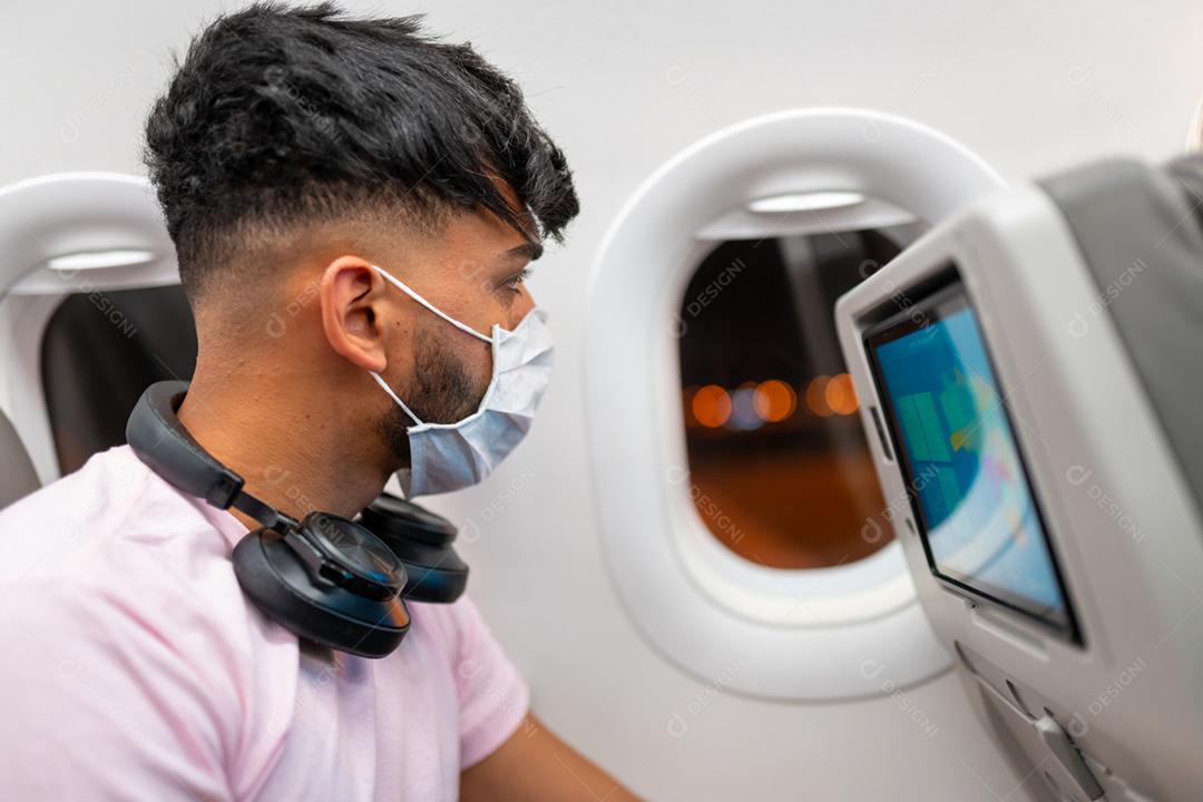 jovem latino-americano usando máscara facial protetora, viajando de avião. Nova viagem normal após o conceito