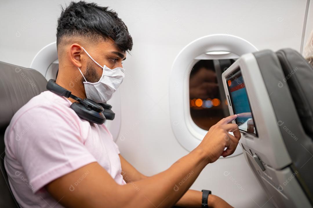 jovem latino-americano usando máscara facial protetora, viajando de avião. Nova viagem normal após o conceito