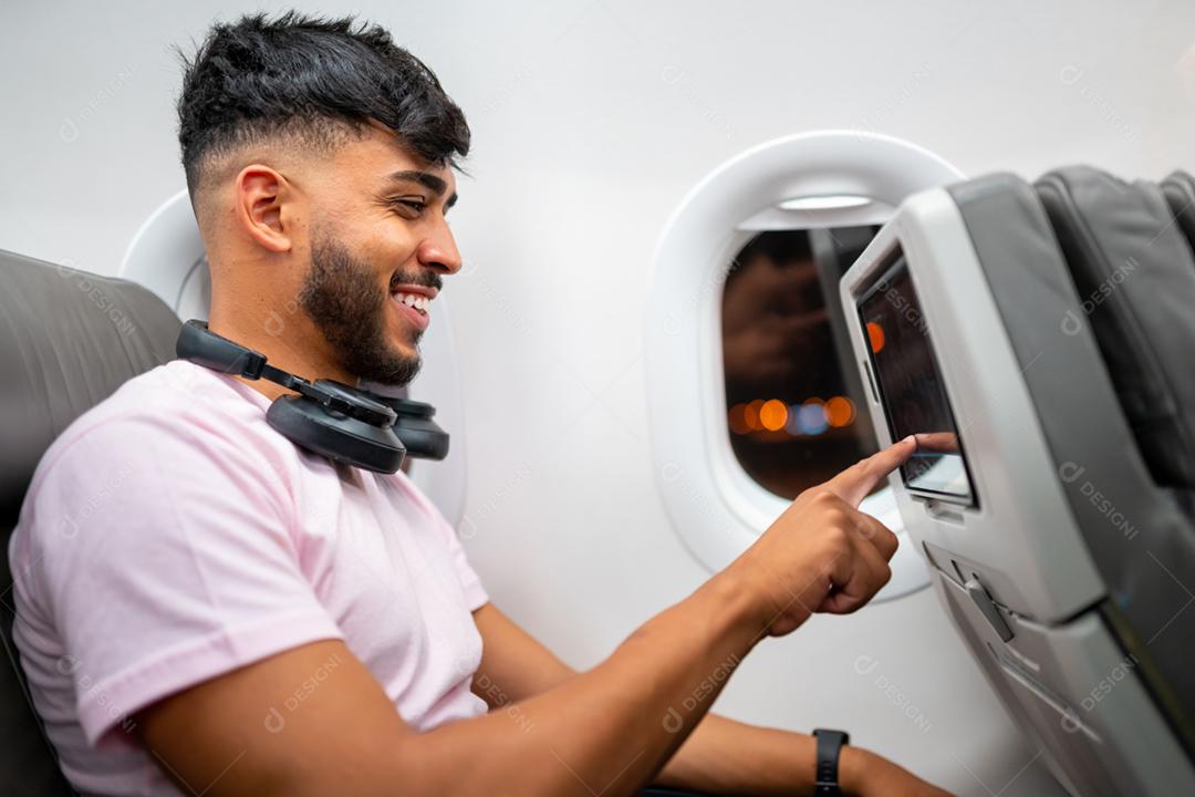 Passageiro no avião tocando a tela de entretenimento LCD. Homem latino-americano na cabine do avião