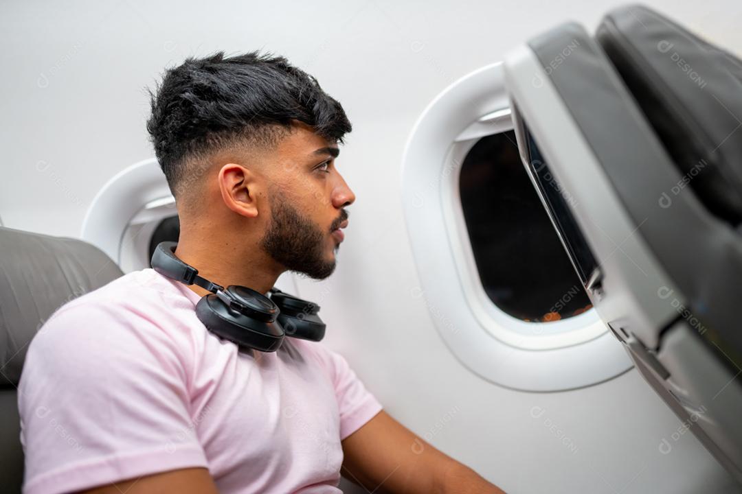 Passageiro no avião, olhando para a janela. Homem latino-americano na cabine do avião, com fones de ouvido.