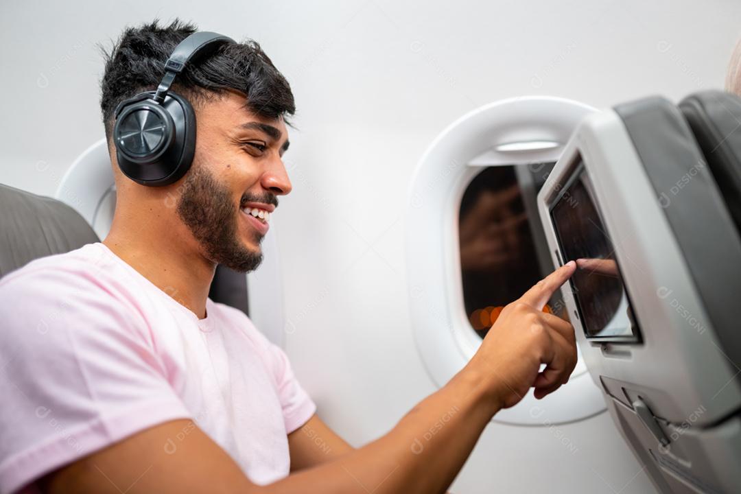 Passageiro no avião tocando a tela de entretenimento LCD. Homem latino-americano na cabine de avião