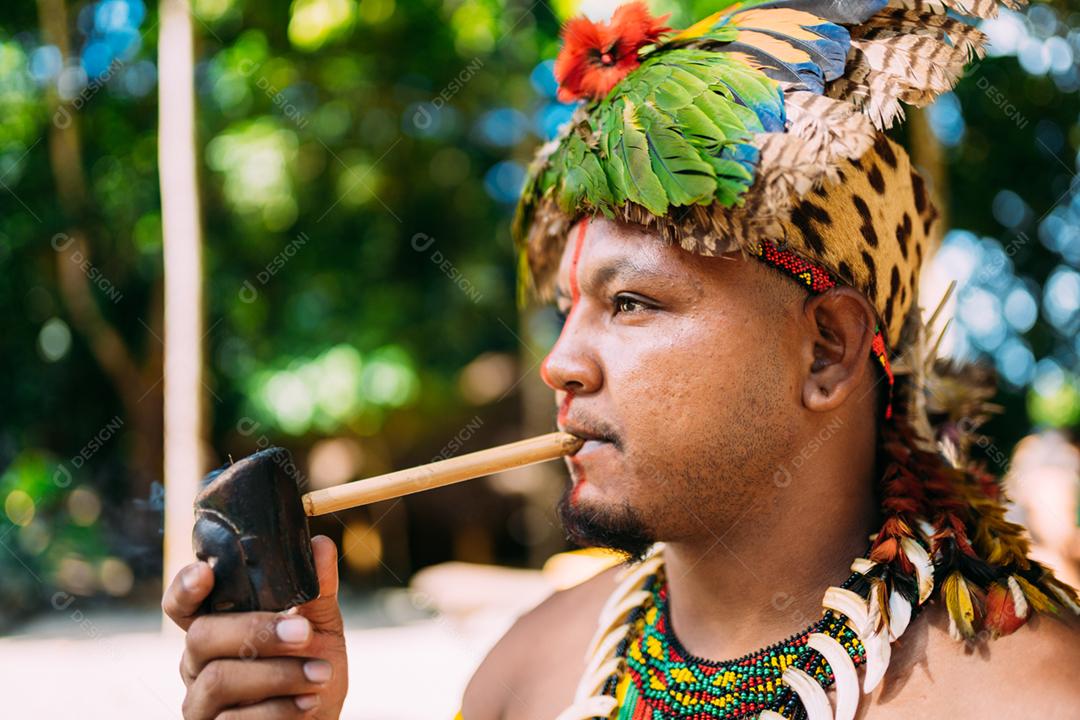 Chefe índio da tribo Pataxó fumando cachimbo. Índio brasileiro com cocar de penas e colar